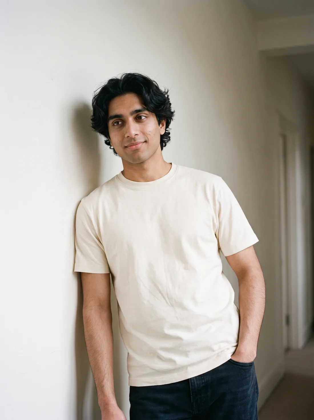 A man in a cream tee leaning against a plaster wall