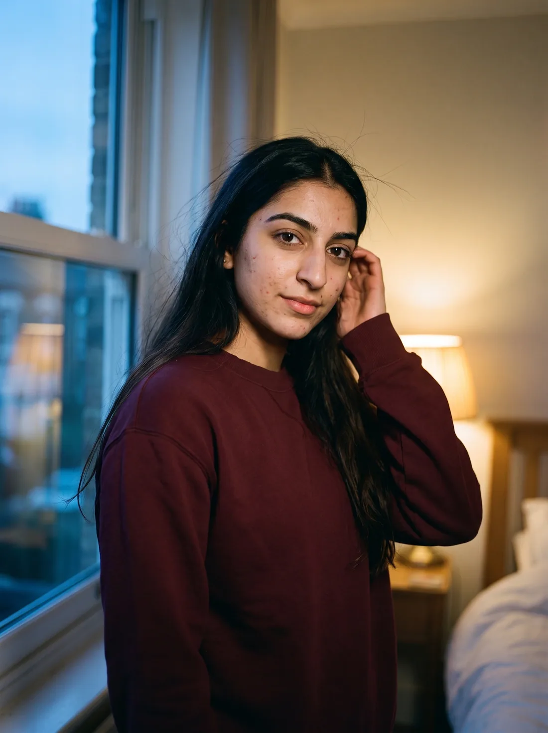 A woman in a maroon sweatshirt by a window at dusk